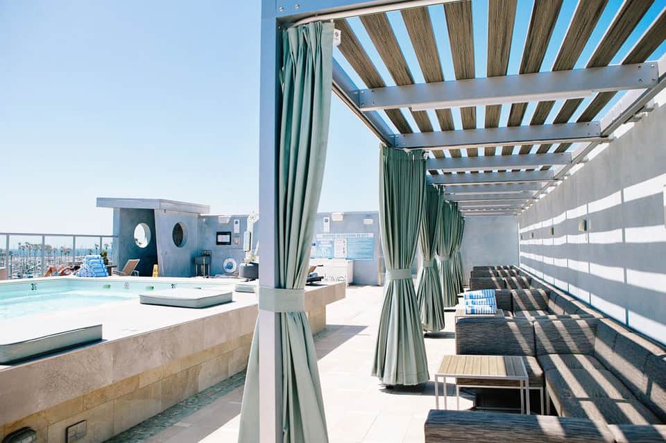 Rooftop pool deck with pergola shade structures, lounge seating, and city skyline views