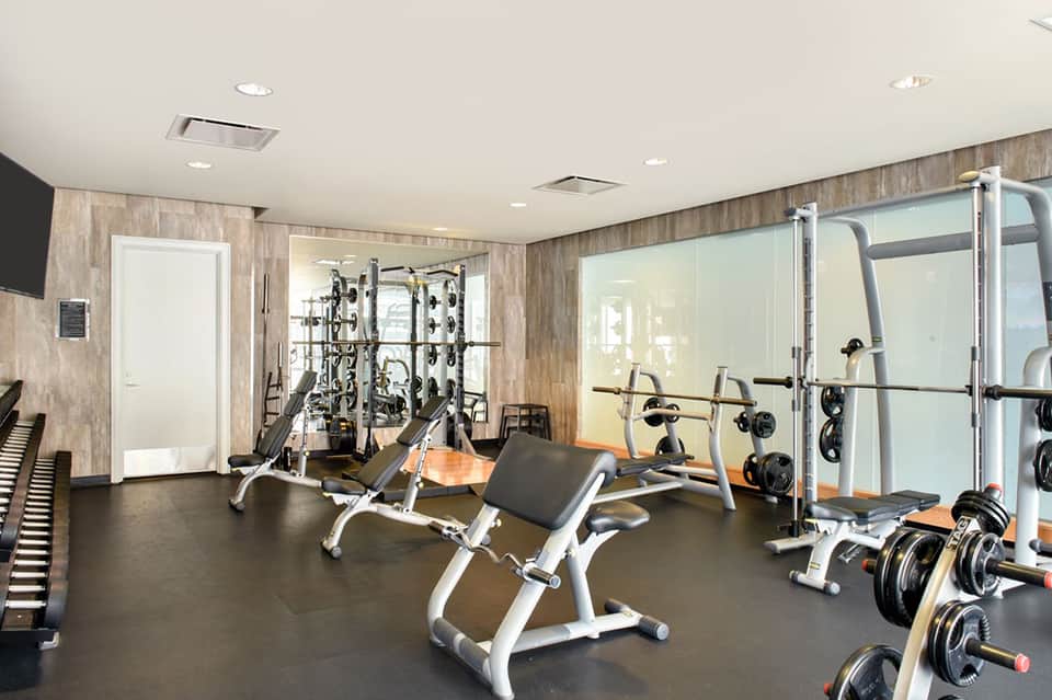 Modern fitness center with weight machines, dumbbells, equipment rack, and glass partition wall