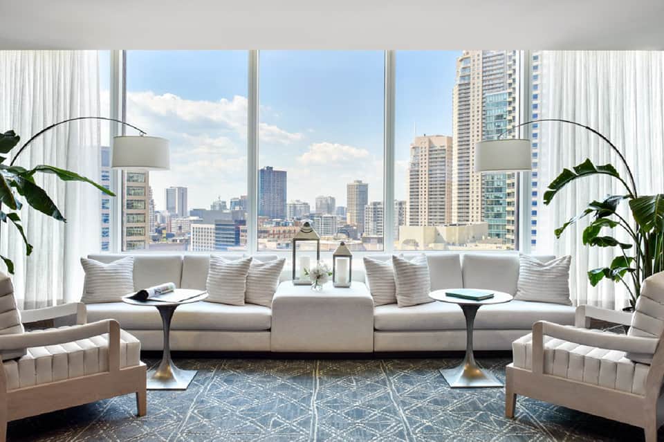 Contemporary hotel lounge with white seating, arc lamps, and city skyline views through floor-to-ceiling windows