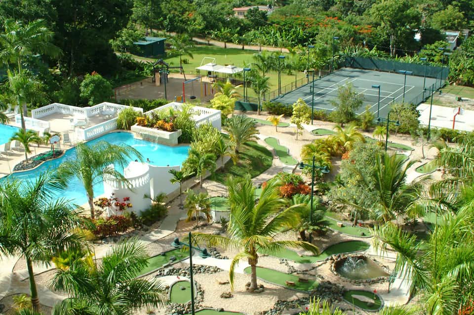 Aerial view of resort with curved pool, mini golf course, and palm trees