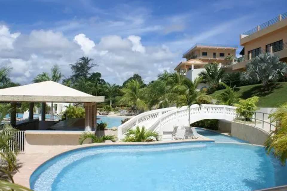 Curved resort pool with cabana, lush tropical landscaping, and Mediterranean-style villa in background