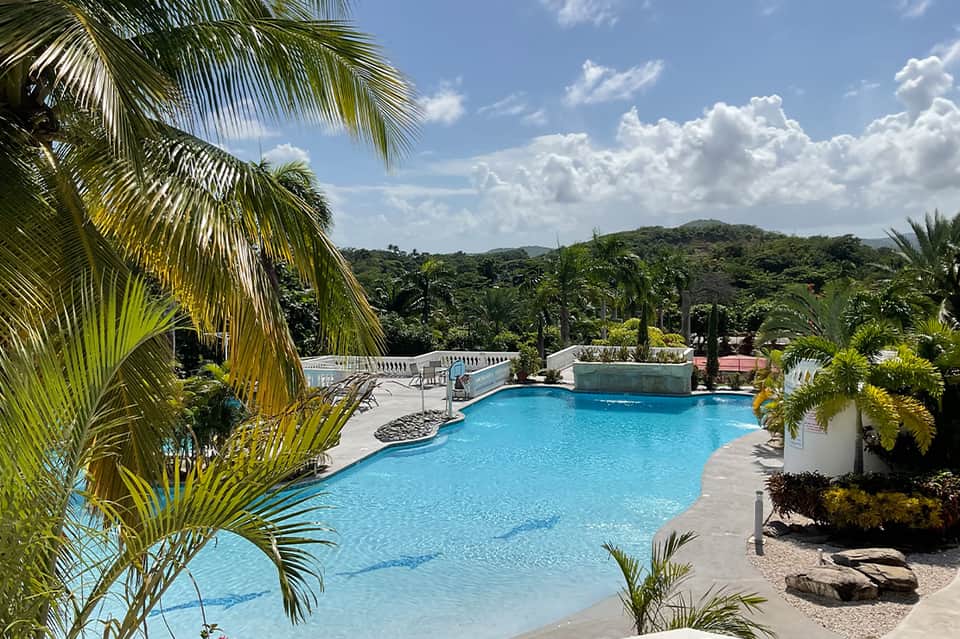 Resort pool surrounded by tropical palms, mountains in background, bright turquoise water