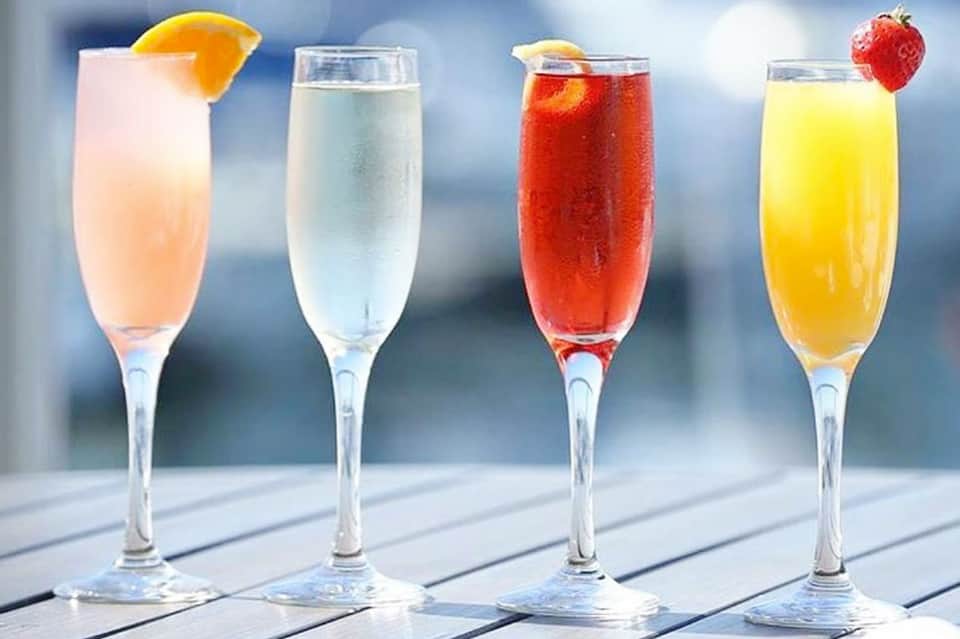 Four colorful cocktails with garnishes displayed on a white deck in bright sunlight