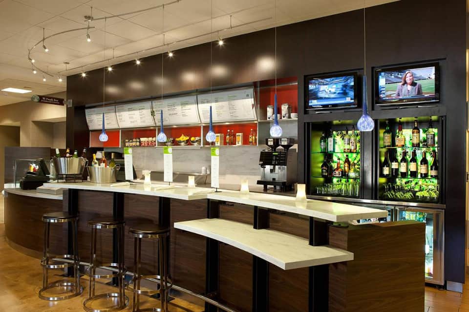 Modern hotel bar with dark wood counter, pendant lighting, and beverage display refrigerators