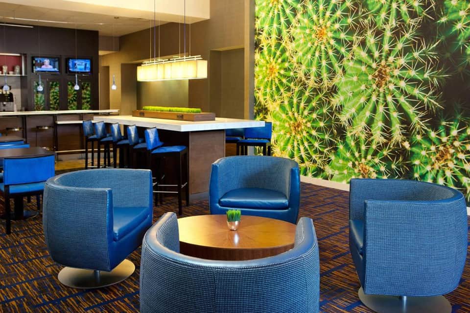Modern hotel lounge with blue accent chairs, green living wall, bar counter, and contemporary design