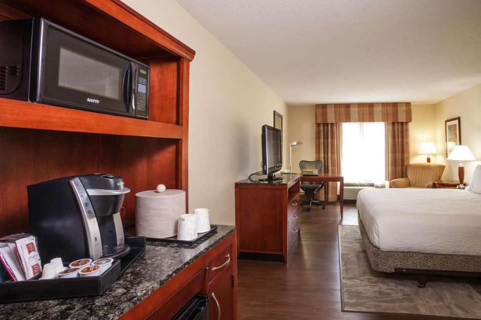 Hotel room interior with queen bed, wood furnishings, coffee maker, and modern amenities