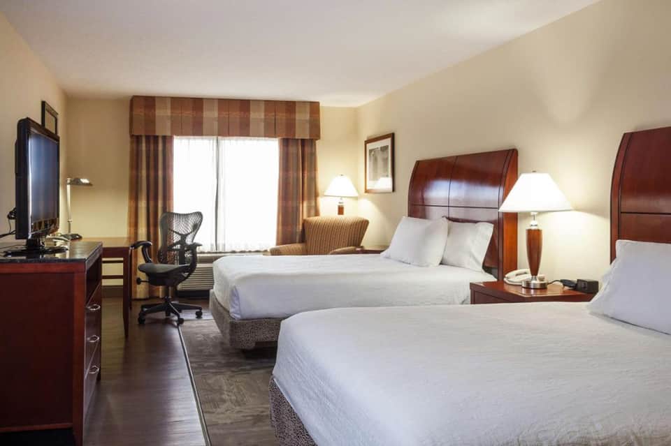 Spacious hotel room with two double beds, desk, and large windows with city views