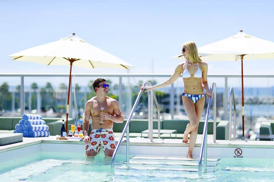Couple relaxing by modern pool with umbrellas and city skyline