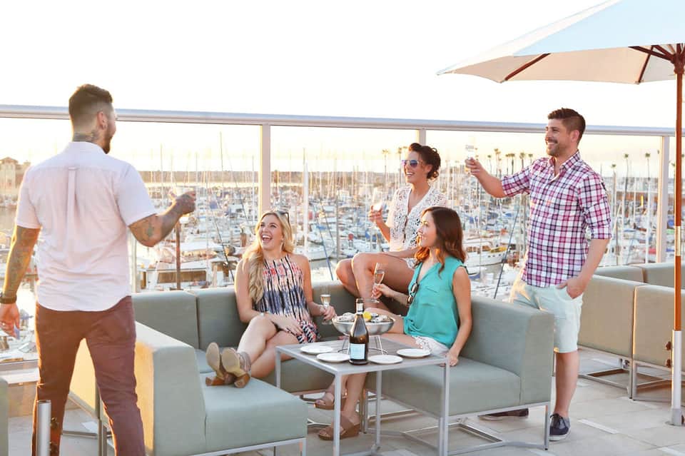 Group of friends enjoying drinks on a rooftop terrace overlooking a marina with sailboats