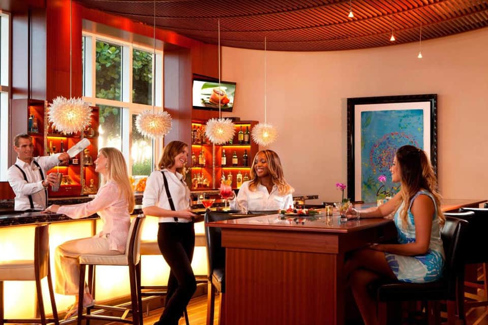 Upscale bar lounge with coral walls, hanging lights, and guests dining