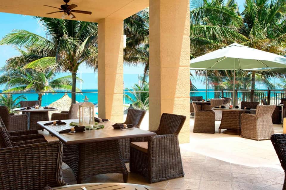 Oceanfront terrace with wicker dining chairs, white umbrellas, columns, and turquoise sea view