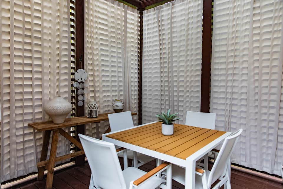 Private outdoor patio with wooden dining table, white chairs, and geometric wall panels