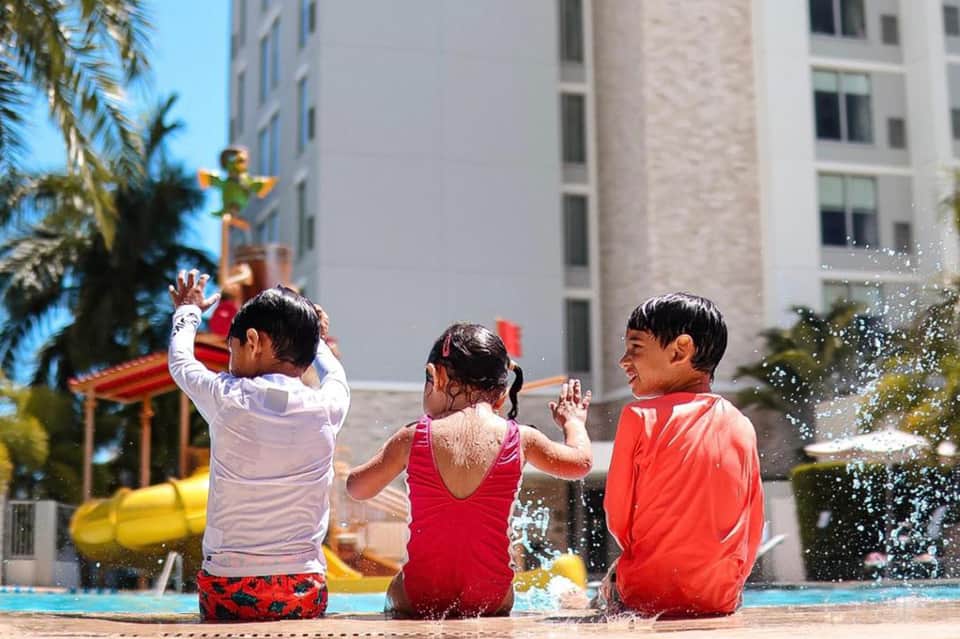 Children playing in shallow pool water with splash, surrounded by tall residential buildings