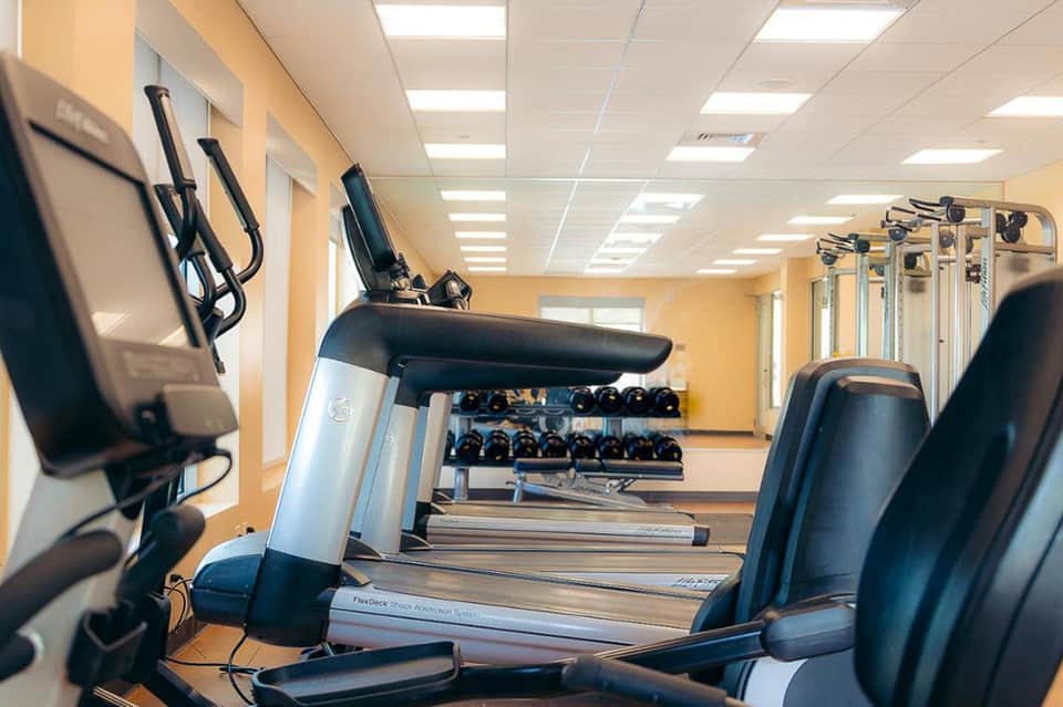 Fitness center with treadmills, exercise bikes, dumbbells, and yellow walls under fluorescent lighting