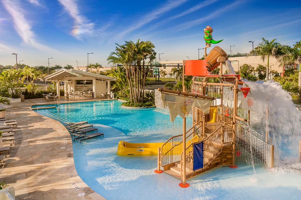 Family pool area with colorful water play structures, pirates ship theme, shallow pool, cabana, and palm landscaping