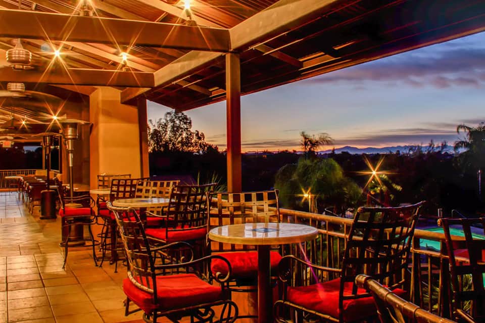 Twilight terrace with lounge seating, glowing string lights, wooden pergola, and scenic sunset views