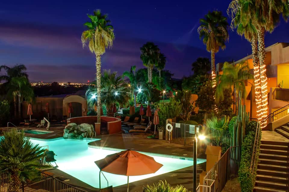 Resort pool at twilight with glowing palm trees, tiki torches, and resort buildings