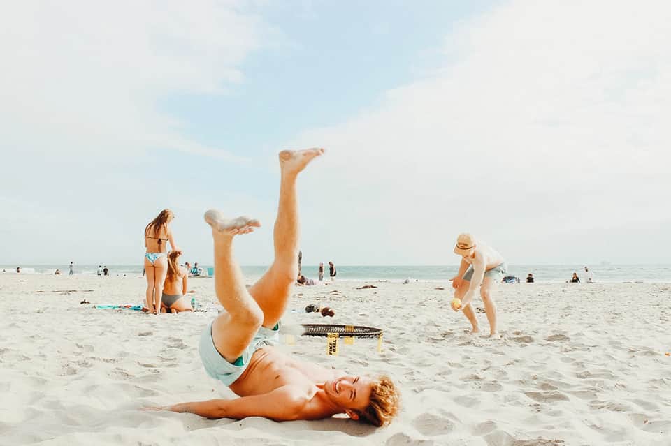 Man doing handstand on sandy beach with ocean and beach volleyball in background