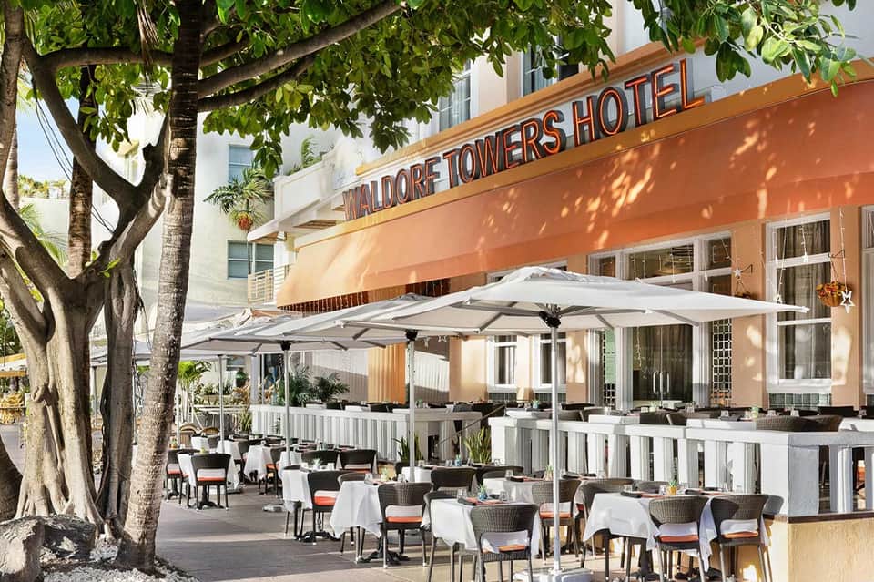 Hotel terrace dining area with white umbrellas, coastal palm trees, and casual seating