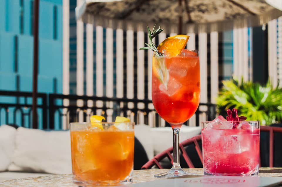 Tropical cocktails on beachfront table with white fence and thatched umbrellas