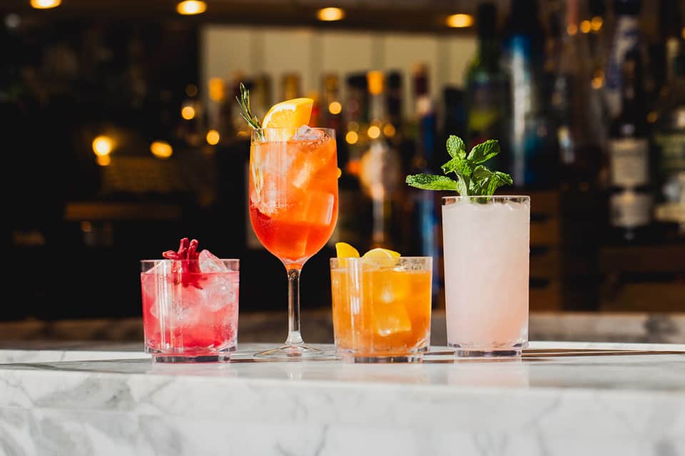 Craft cocktails at bar with colorful drinks, citrus garnish, and ambient lighting