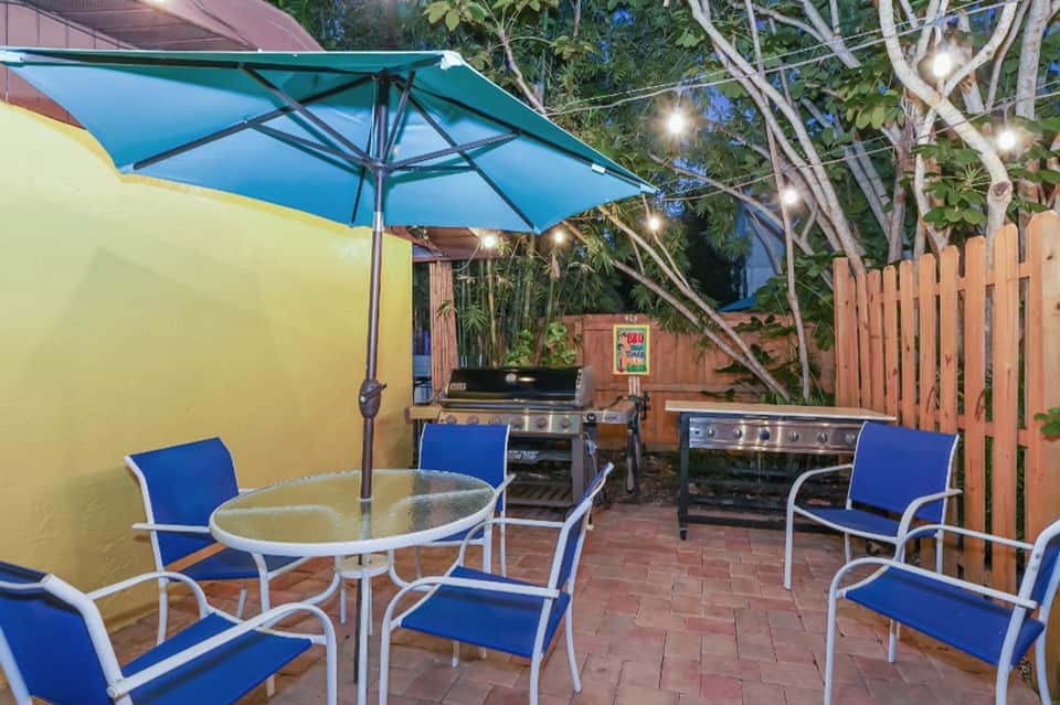 Backyard patio with blue umbrella, grill station, dining table, and string lights