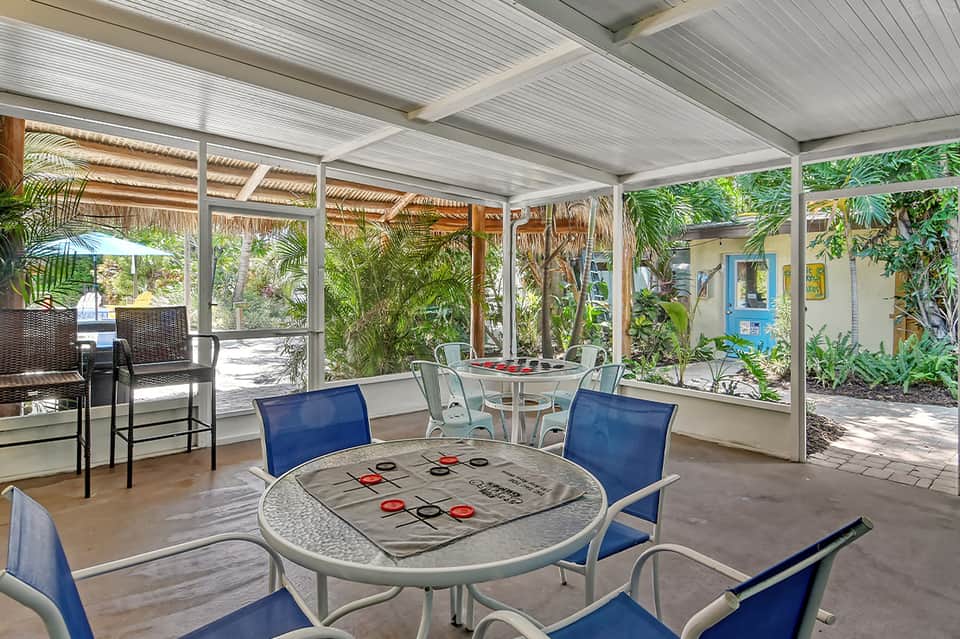 Covered patio lounge area with tic-tac-toe table, chairs, and tropical vegetation views