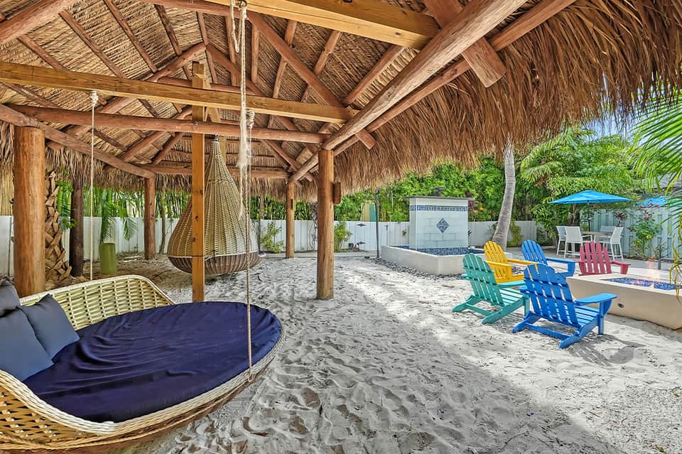 Beach cabana with woven hammock, colorful Adirondack chairs, and thatched roof