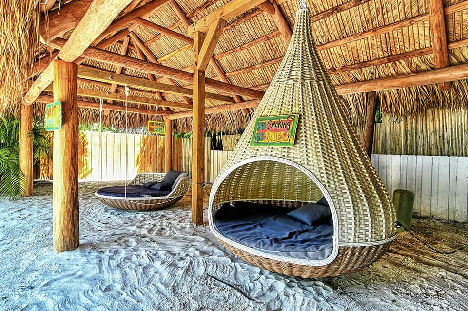 Beach cabanas with woven pods and lounge beds under wooden thatched roof structures