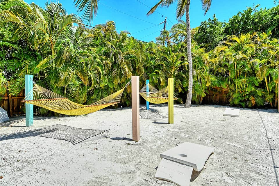 Beach area with yellow hammocks, palm trees, and cornhole game setup