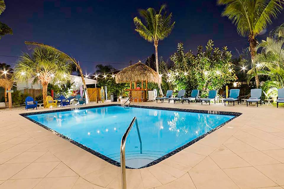 Diamond-shaped resort pool illuminated at night surrounded by palm trees and lounge chairs