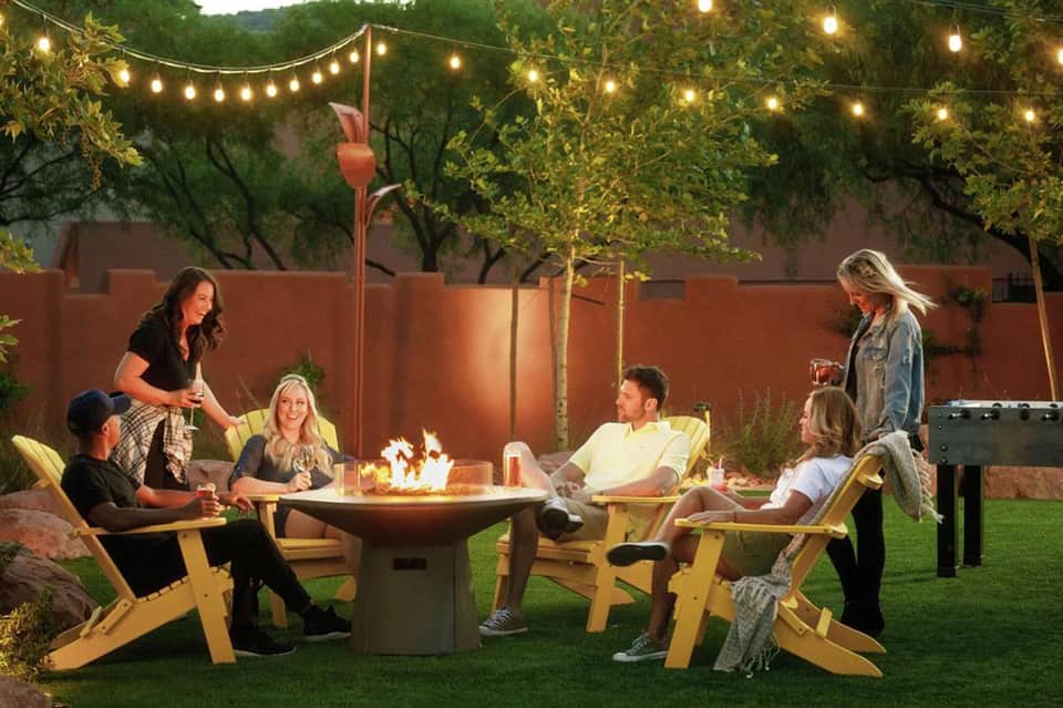 Outdoor gathering around fire pit with string lights and adirondack chairs at dusk