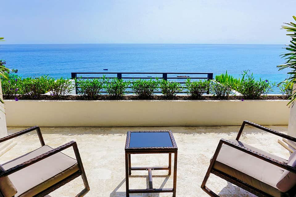 Oceanfront lounge area with black lounge chairs, blue cushions, and pristine sea view