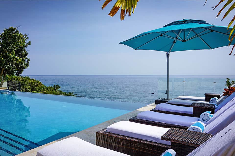Infinity pool overlooking the ocean with lounge chairs and turquoise umbrella