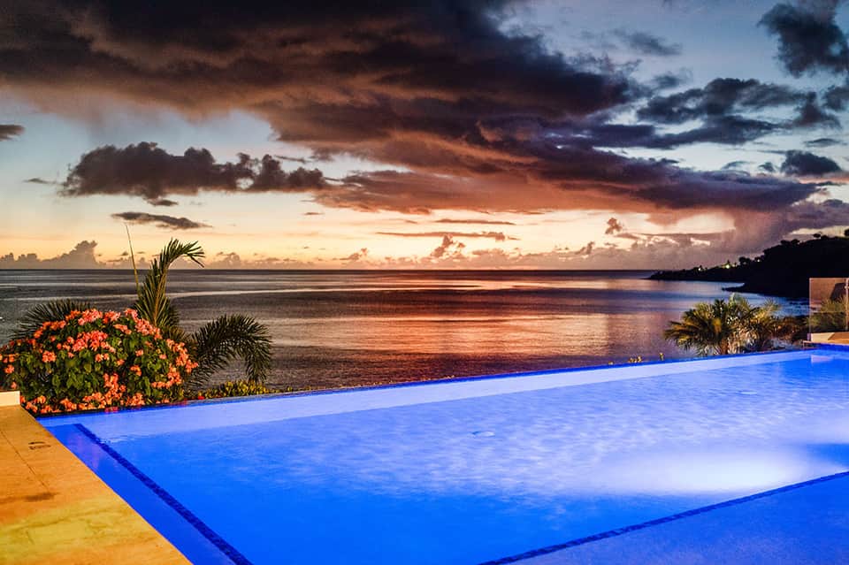 Infinity pool overlooking ocean at dramatic sunset with palm trees and colorful sky