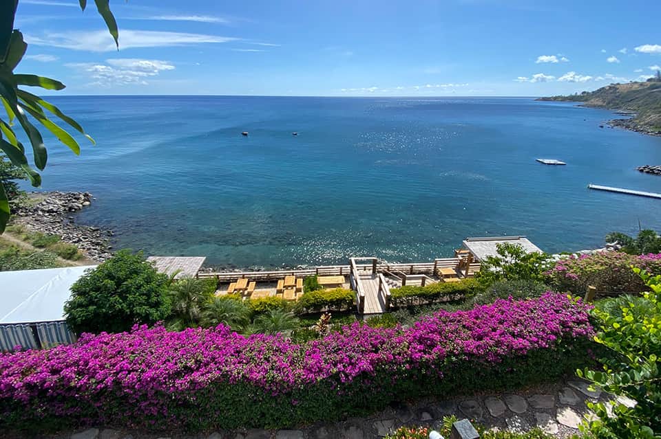 Oceanfront terrace with wooden lounge chairs, magenta bougainvillea flowers, and blue water