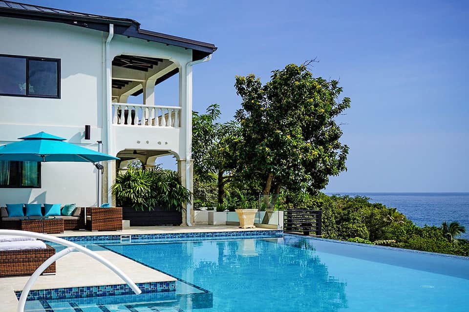Oceanfront villa with infinity pool, white architecture, turquoise umbrella, and sea views