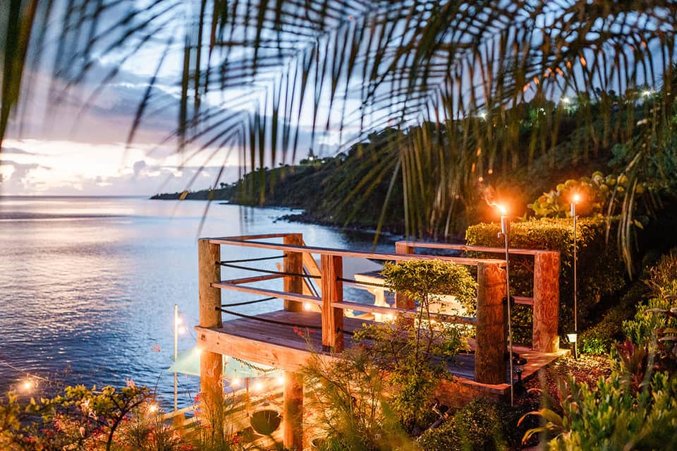 Illuminated wooden deck over tropical water at sunset with palm trees and mangroves