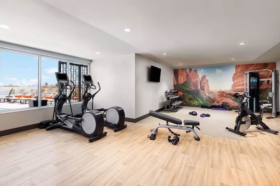 Modern fitness center with elliptical machines, stationary bikes, weights, and desert landscape mural