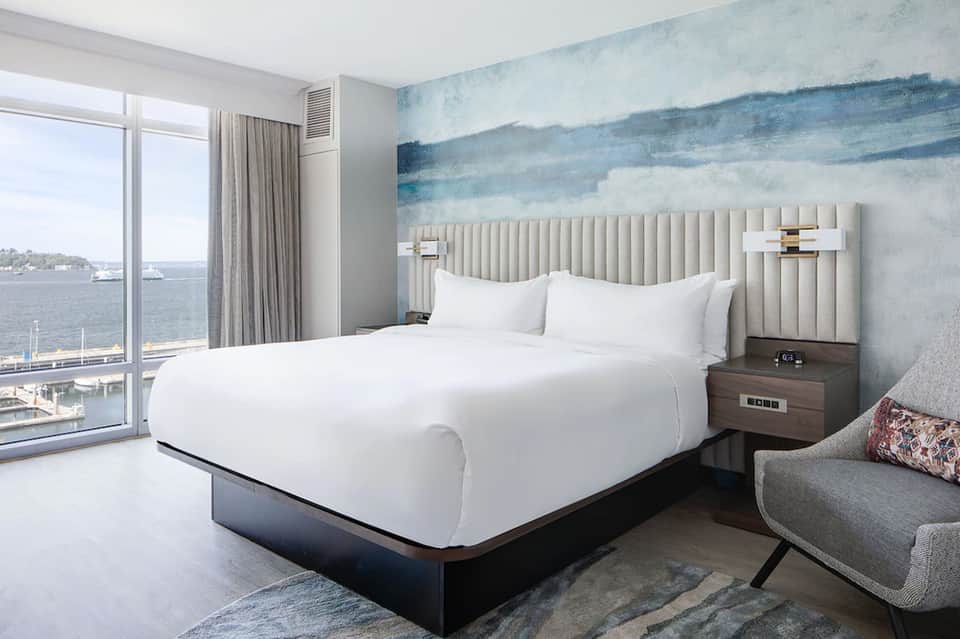 Waterfront hotel room with white bed, striped headboard, ocean view, and contemporary furnishings