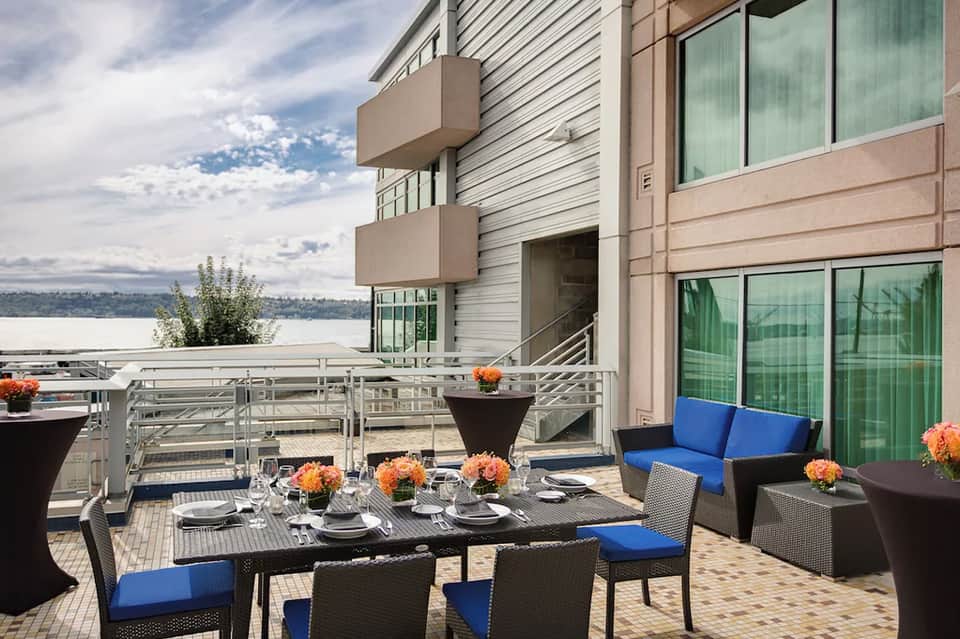 Waterfront dining table set with orange flowers, blue cushioned seating, and lake or bay views