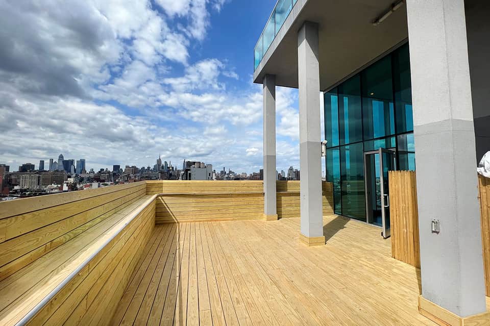 Wooden rooftop deck with city skyline view, modern glass doors, and white columns