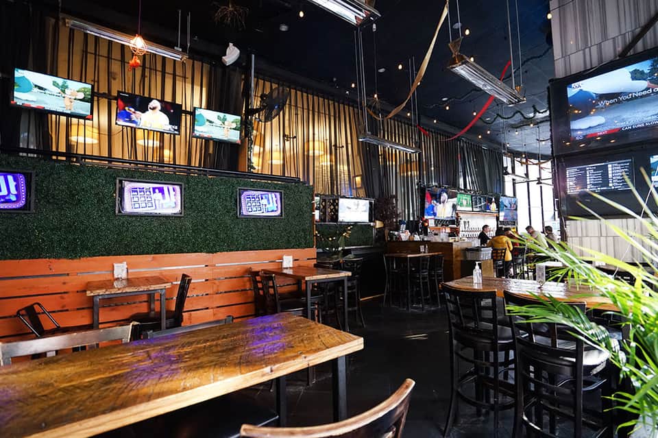 Modern sports bar interior with wooden tables, neon signs, and TV screens