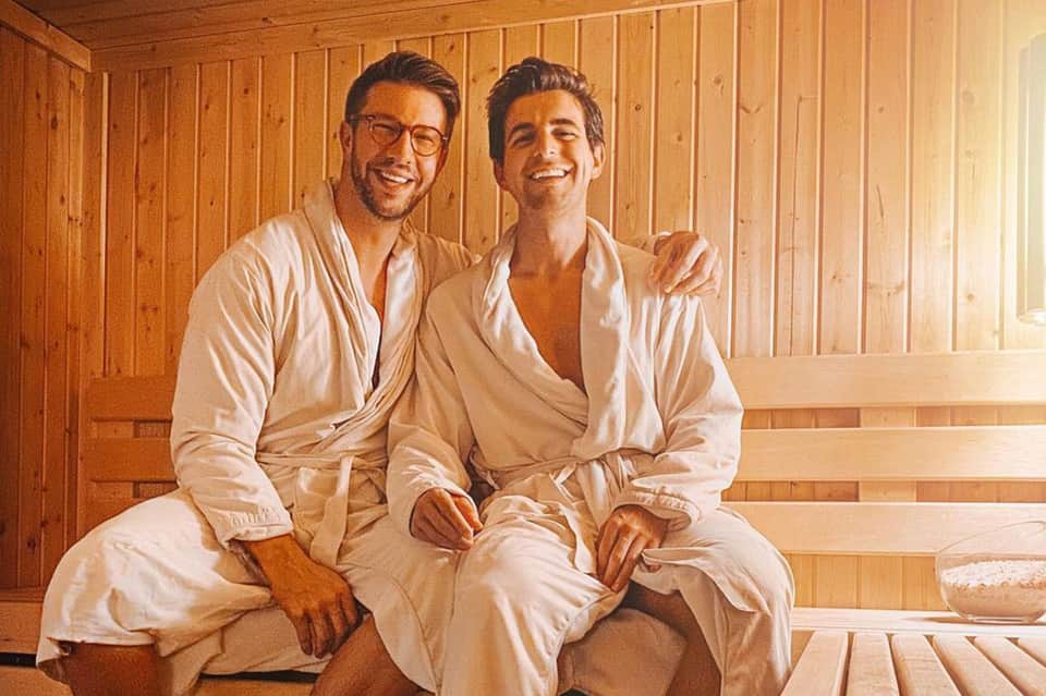 Two men in white robes sitting in wooden sauna interior