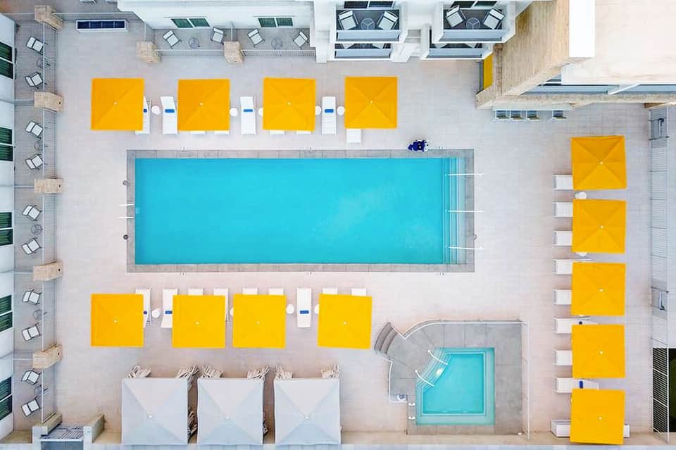Aerial view of hotel pool deck with bright yellow umbrellas and turquoise swimming pool surrounded by lounge chairs