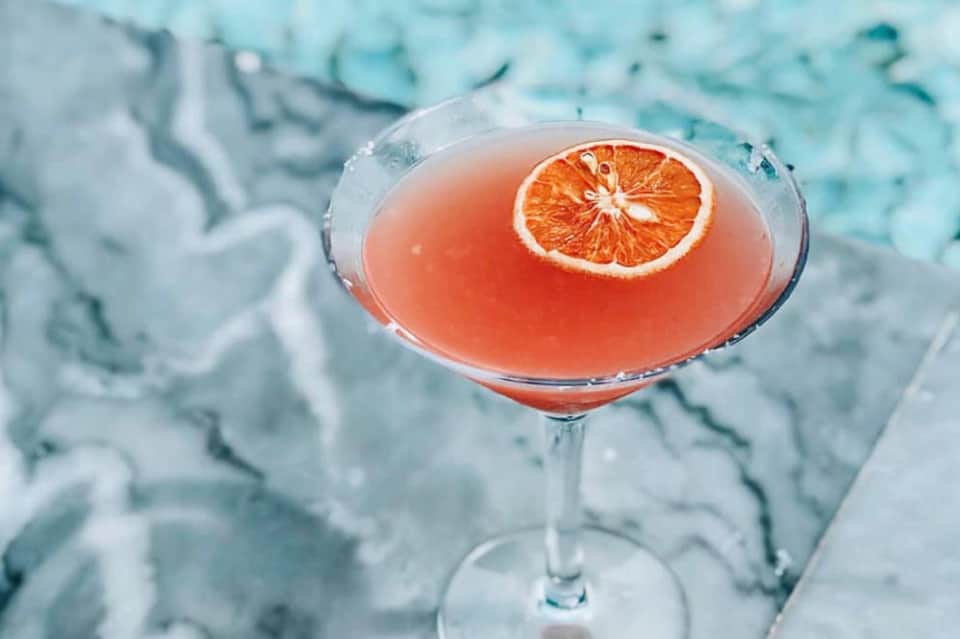 Grapefruit cocktail with orange slice garnish on ice at poolside lounge