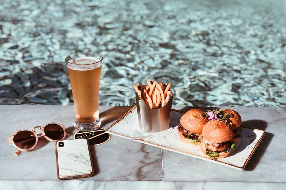 Cold beer and gourmet sliders with fries at beachside table near water