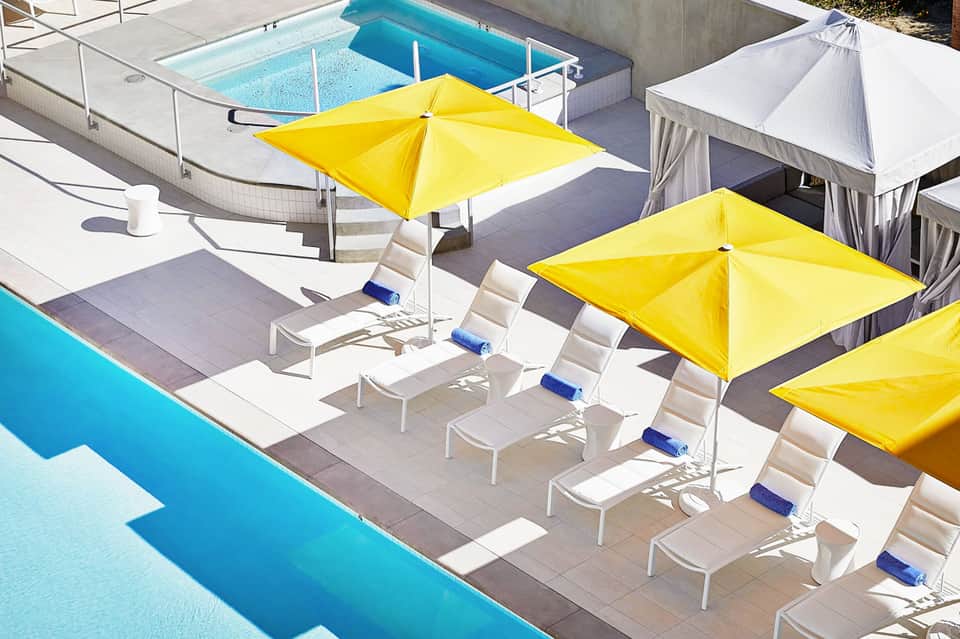 Luxury poolside lounge area with yellow umbrellas, white chairs, and blue swimming pools on sunny day