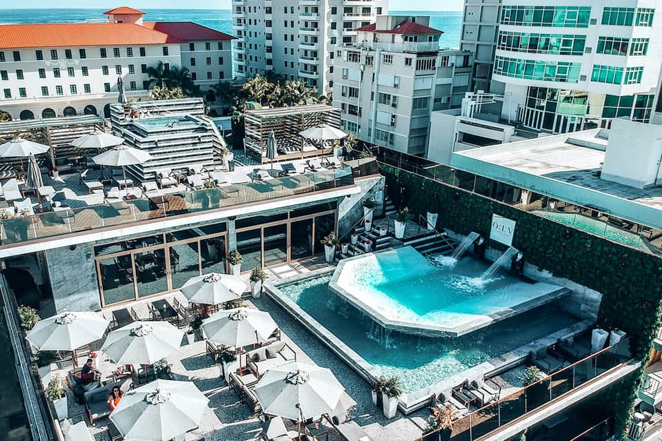 Aerial view of rooftop pool and lounging deck surrounded by beachfront high-rise hotel buildings