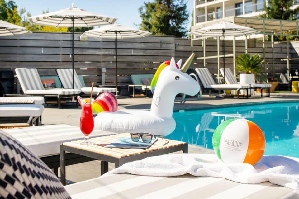 Resort pool area with unicorn float, lounge chairs, umbrellas, and colorful drinks